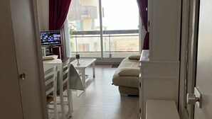Une chambre à coucher avec un lit, un bureau avec un ordinateur, une fenêtre avec des rideaux et un balcon.