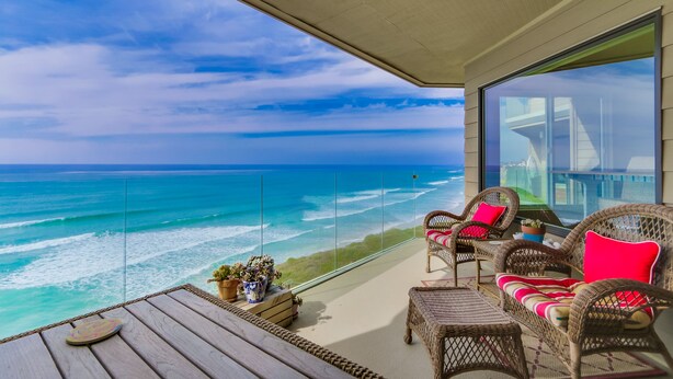 A balcony with wicker furniture, a wooden table, and a view of the ocean. - Oceanfront Balcony with Heated Pool & Hot Tub (Solana Beach)