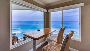 A room with a view of the ocean, a wooden table, and wicker chairs. - Oceanfront Balcony with Heated Pool & Hot Tub (Solana Beach)