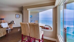 A room with wicker chairs, a small table, and a view of the ocean through large windows. - Oceanfront Balcony with Heated Pool & Hot Tub (Solana Beach)