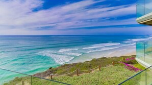 A coastal view from a balcony with a clear sky, ocean waves, and a grassy area with a fence. - Oceanfront Balcony with Heated Pool & Hot Tub (Solana Beach)