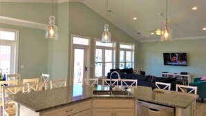 A kitchen with granite countertops, white cabinets, and a built-in dishwasher. There is a dining area with wooden chairs and a table. - GREAT OCEAN VIEWS -- 5 Bedroom, 5.5 Bath, 2 Living Rooms (Ocean Isle Beach)