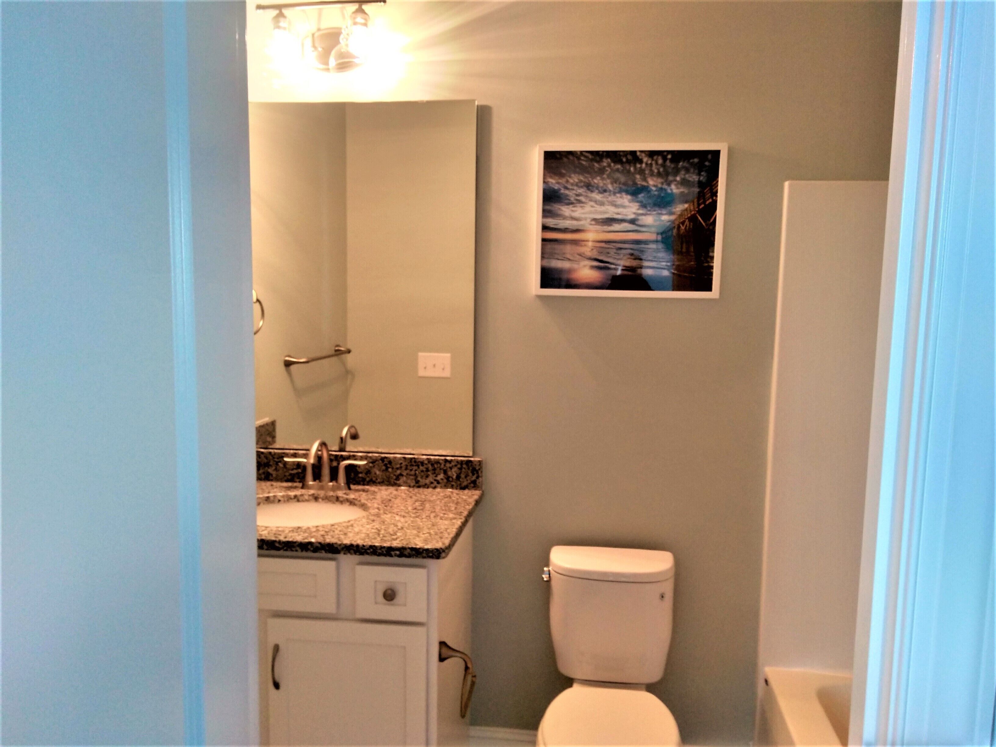 A bathroom with a sink, mirror, toilet, and a framed picture on the wall.