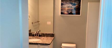 A bathroom with a sink, mirror, toilet, and a framed picture on the wall.