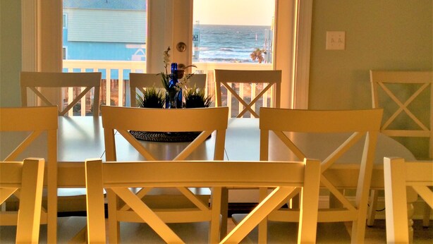 A dining area with a view of the ocean, featuring a table with chairs and a vase with flowers. - GREAT OCEAN VIEWS -- 5 Bedroom, 5.5 Bath, 2 Living Rooms (Ocean Isle Beach)
