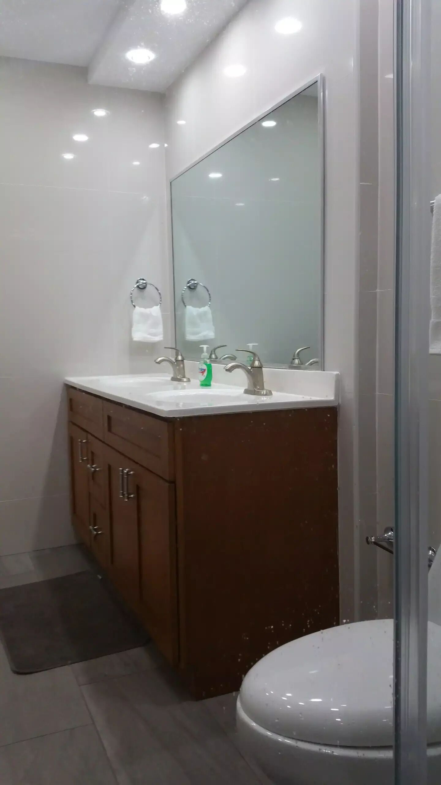 Un baño moderno con cabina de ducha de vidrio, un espejo grande y un mueble de tocador con lavabo y dos grifos.