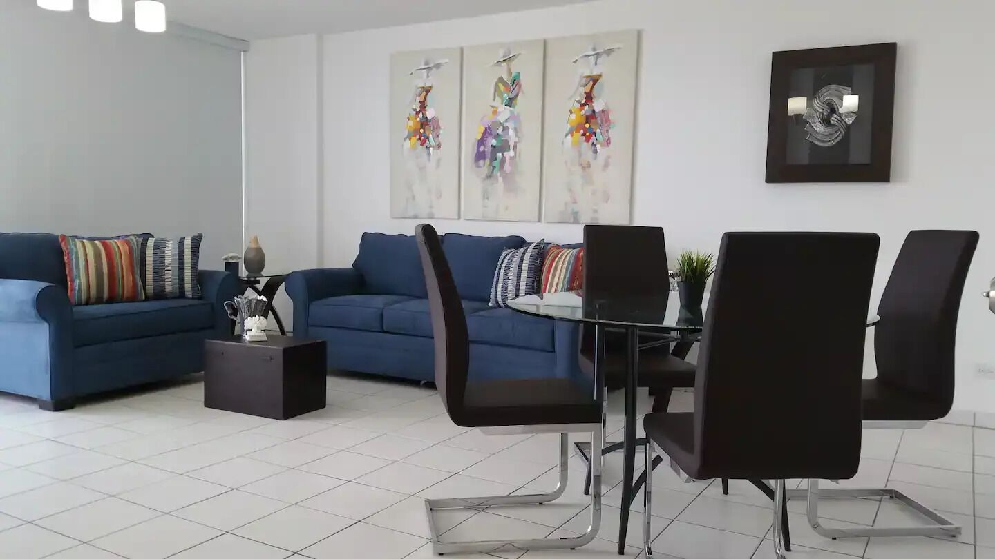 Una sala de estar moderna con un sofá azul, una mesa de comedor con sillas y arte abstracto en las paredes.