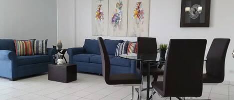 Una sala de estar moderna con un sofá azul, una mesa de comedor con sillas y arte abstracto en las paredes.