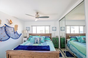 Une chambre avec deux lits, un ventilateur de plafond et un grand miroir.