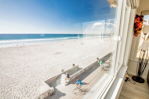 A beach view from a window overlooking a sandy beach with a few people and a clear sky.