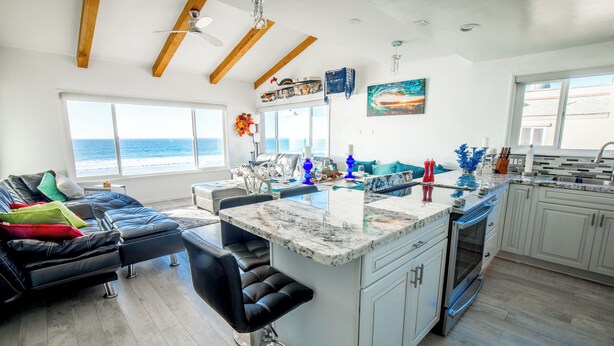 Una cocina moderna con una isla grande, asientos tipo bar y vista al océano.