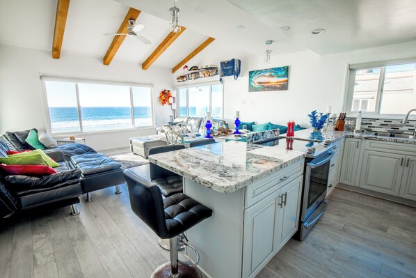 Una cocina moderna con una isla grande, asientos tipo bar y vista al océano.