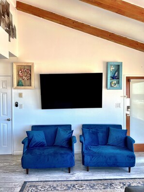 A living room with two blue sofas, a mounted TV, and a wooden ceiling beam.