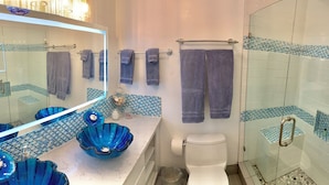 Ein Badezimmer mit einer Duschkabine aus Glas, einer weißen Toilette und einem Waschbecken mit blauen Glasbecken.