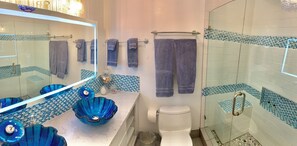 Une salle de bain avec une douche à parois de verre, des toilettes blanches et un lavabo surmonté de deux récipients en verre bleu.