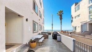 Eine überdachte Terrasse im Freien mit Tischen und Stühlen, einem Mülleimer und einer Palme.
