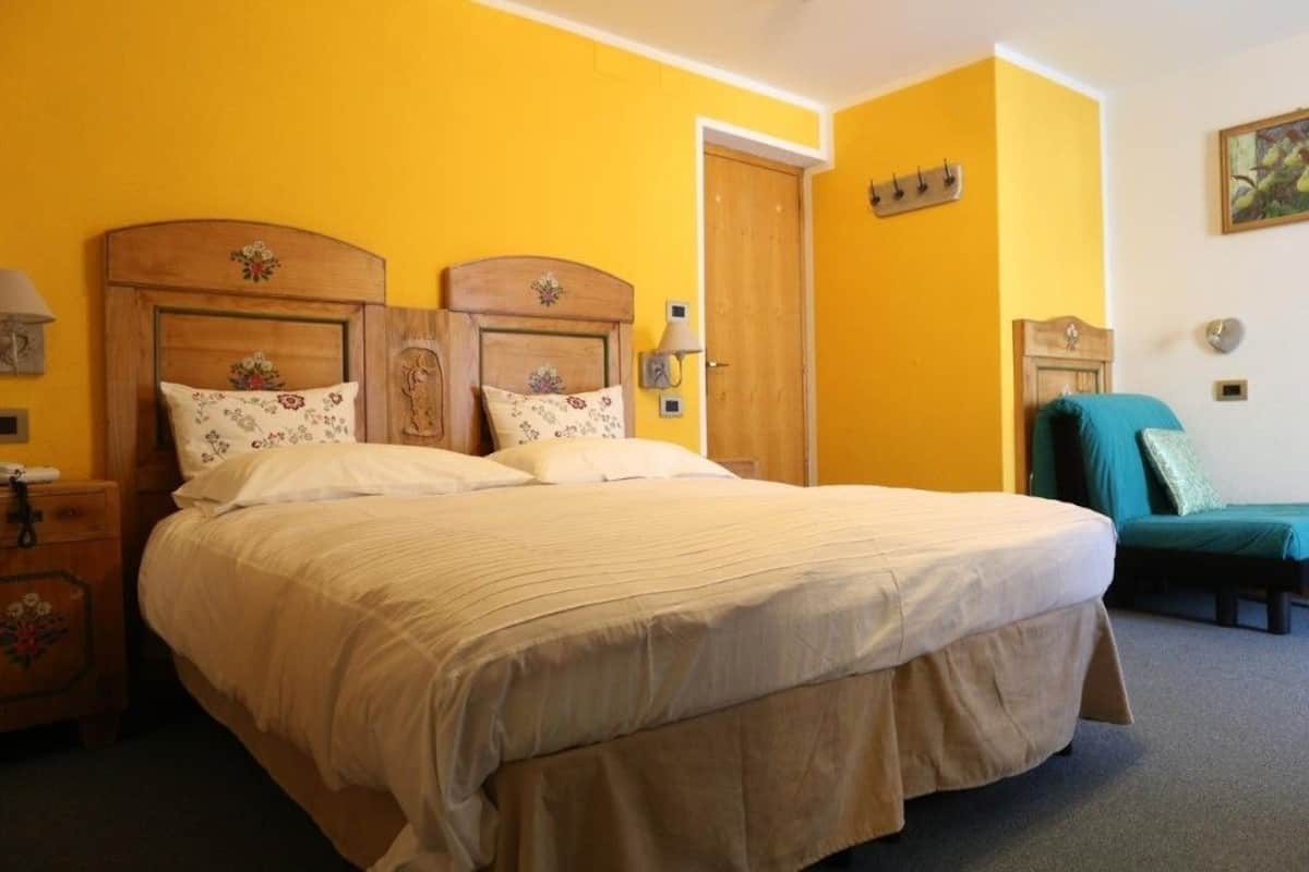 Una habitación con una cama grande, una mesita de noche de madera, una silla verde y una puerta.