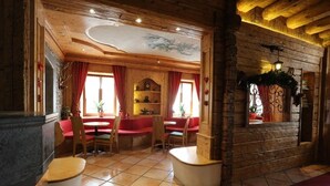 Ein rustikales Interieur mit Holzwänden, einem Fliesenboden und einer Sitzecke mit roten Vorhängen und Holzstühlen.