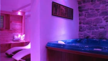 Une salle de spa équipée d’un bain à remous, de bancs en bois et d’un mur en pierre.