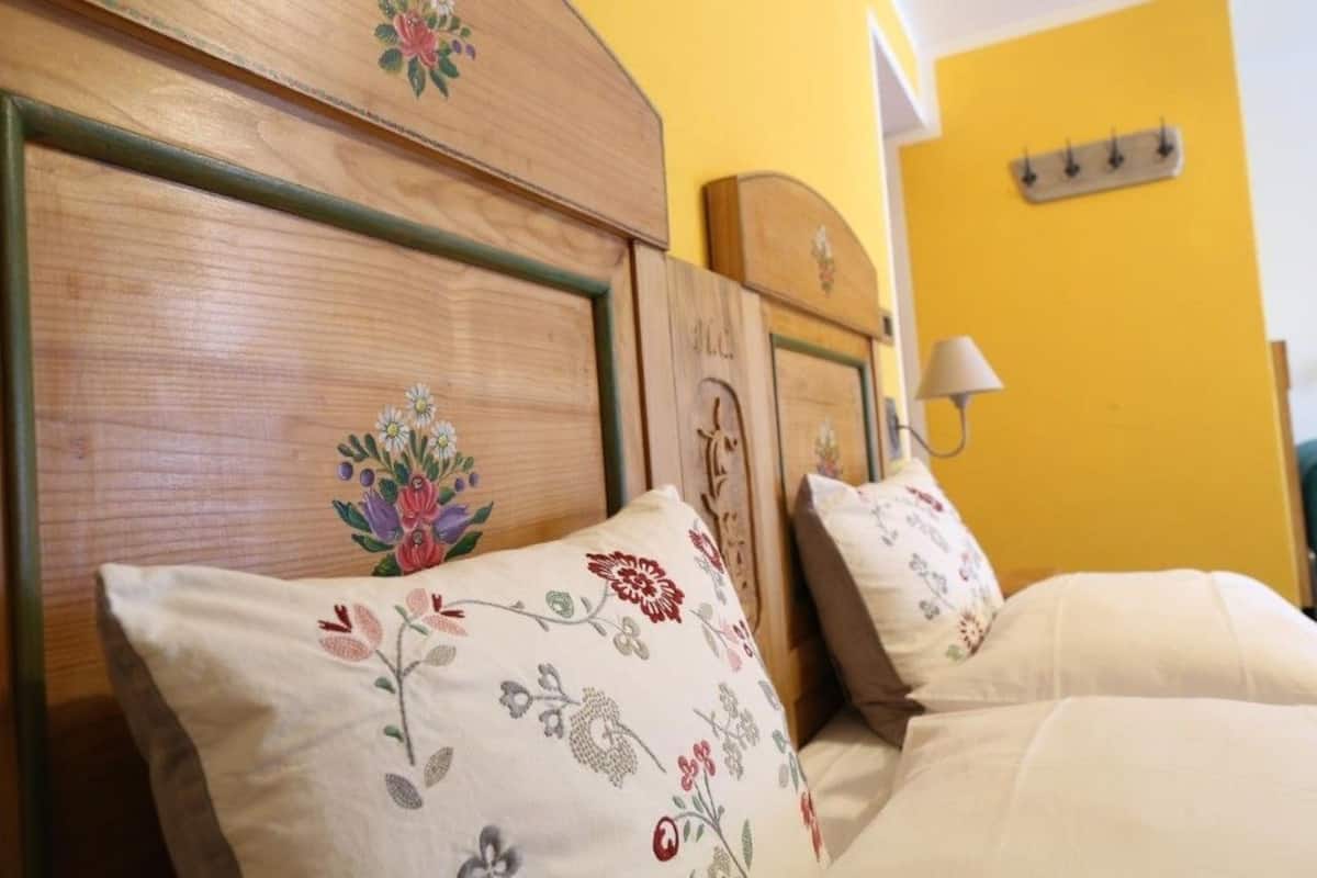 Una cama con almohadas estampadas y un cabecero de madera en una habitación con paredes amarillas.
