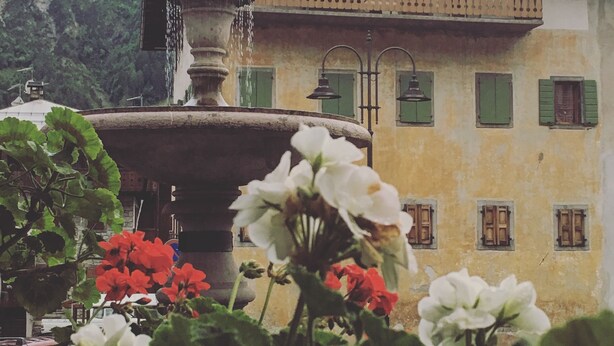 Ein Gebäude mit Balkon, Brunnen und einer Bergkulisse.