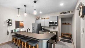 Una cocina moderna con una isla central, taburetes de bar, electrodomésticos de acero inoxidable e iluminación colgante, y un cartel que indica 'MANN TRAIL'.