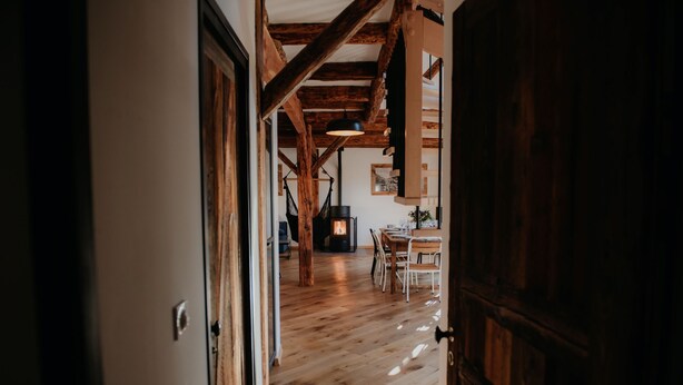Een houten interieur met zichtbare balken, een eethoek en een open haard.