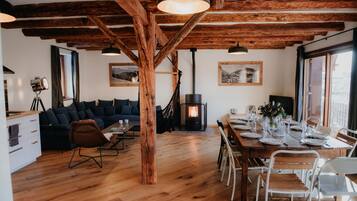 A spacious living area with a wooden ceiling, a sofa set, a dining table set for six, and a fireplace.
