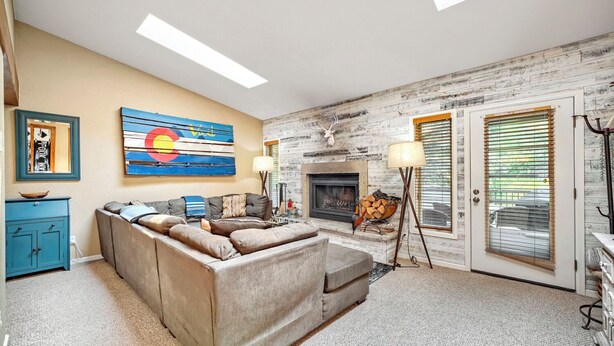 A living room with a fireplace, a sofa, a lamp, and a painting on the wall. - Chic 3-Level Condo w/Private Deck, Hot Tub & BBQ (West Vail)