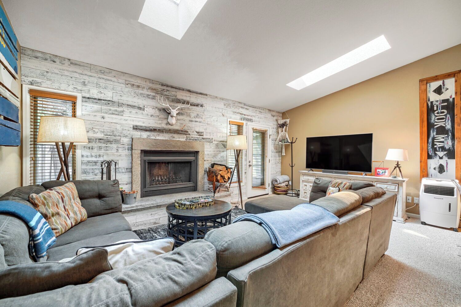 A living room with a fireplace, sofa, TV, and a decorative deer head.