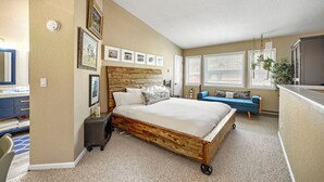 A bedroom with a wooden bed, a blue sofa, a small desk with a mirror, and framed pictures on the wall. - Chic 3-Level Condo w/Private Deck, Hot Tub & BBQ (West Vail)