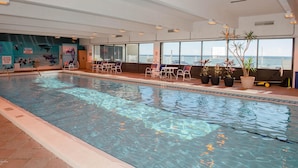 An indoor swimming pool with clear water, surrounded by potted plants and chairs.