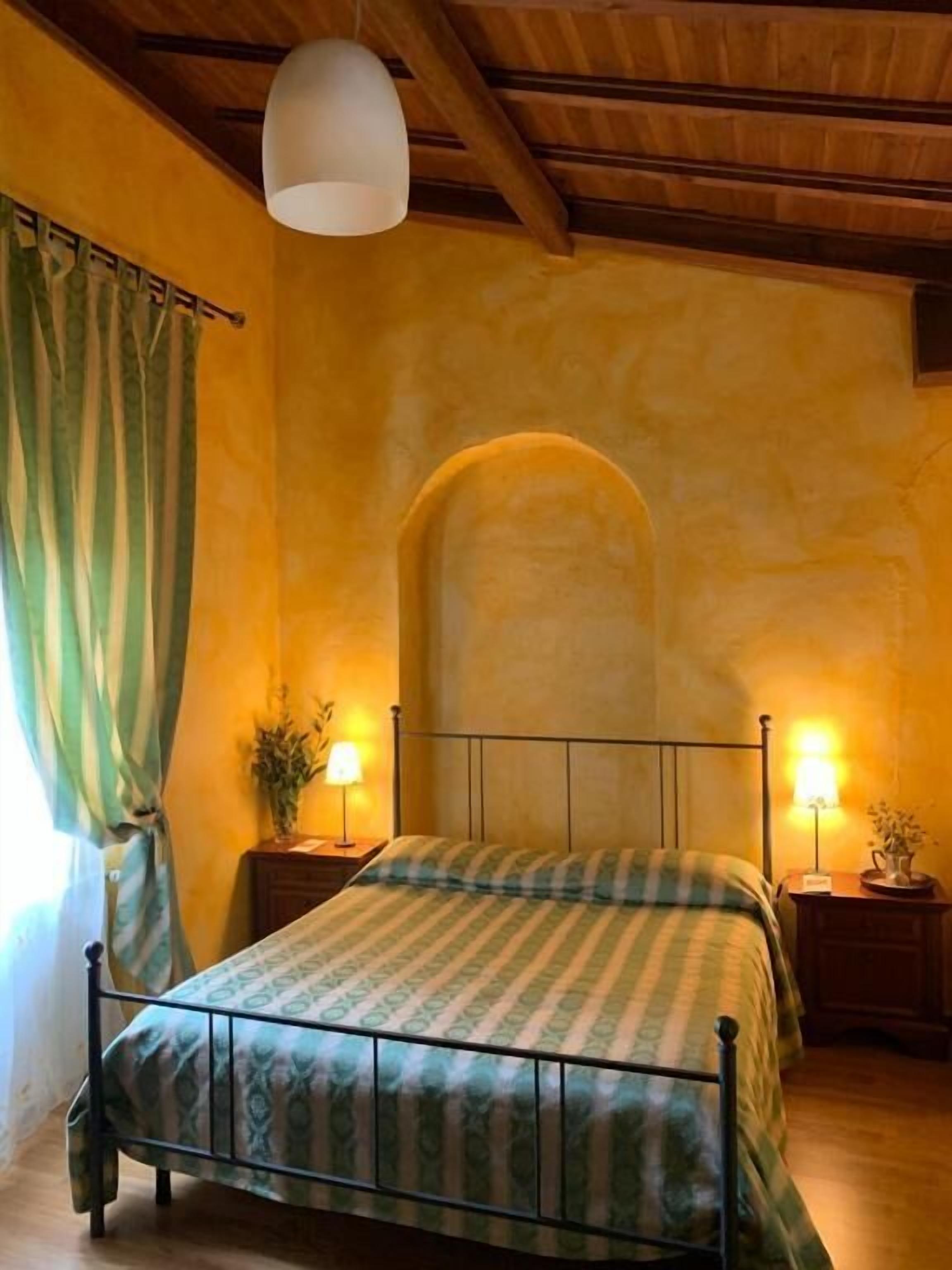 A bedroom with a bed, two bedside tables, a hanging light fixture, and a window with curtains.