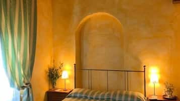 A bedroom with a bed, two bedside tables, a hanging light fixture, and a window with curtains.