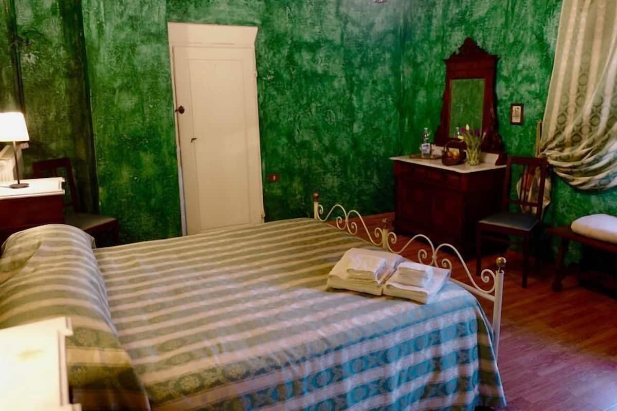A bedroom with a bed, a dresser, a chair, a desk with a lamp, and a mirror.