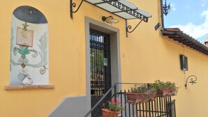 A yellow building with a mural, a staircase, and potted plants. - Barco Mediceo (Carmignano)