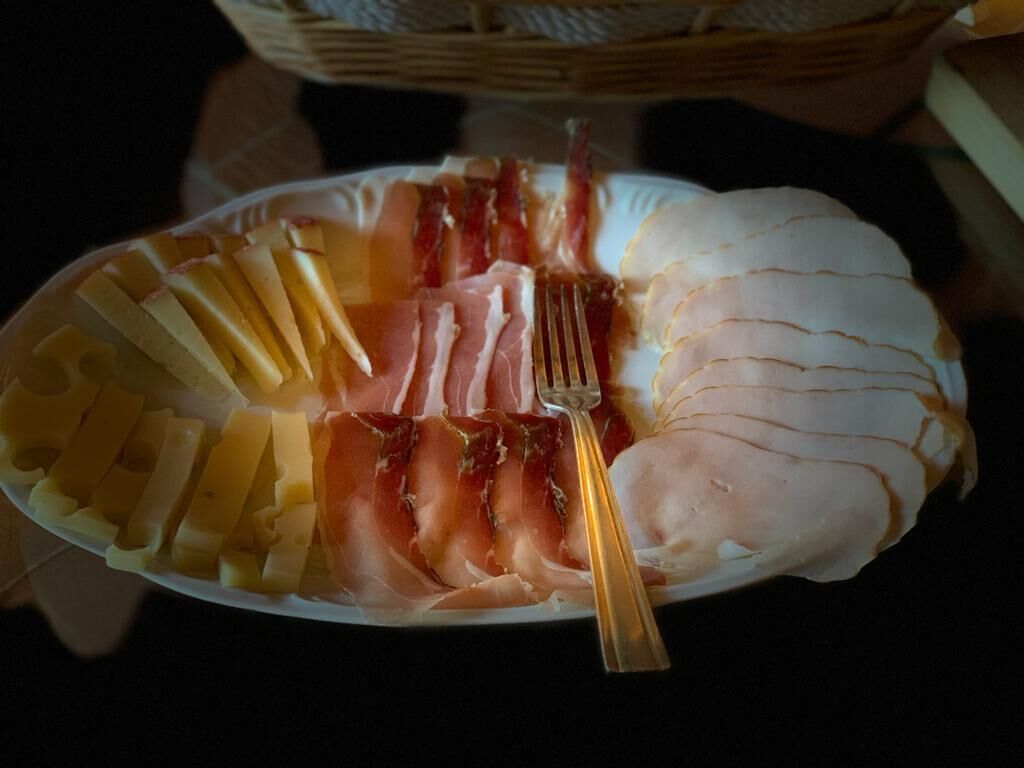 A plate with various types of meat, including ham and bacon, arranged on a white plate.