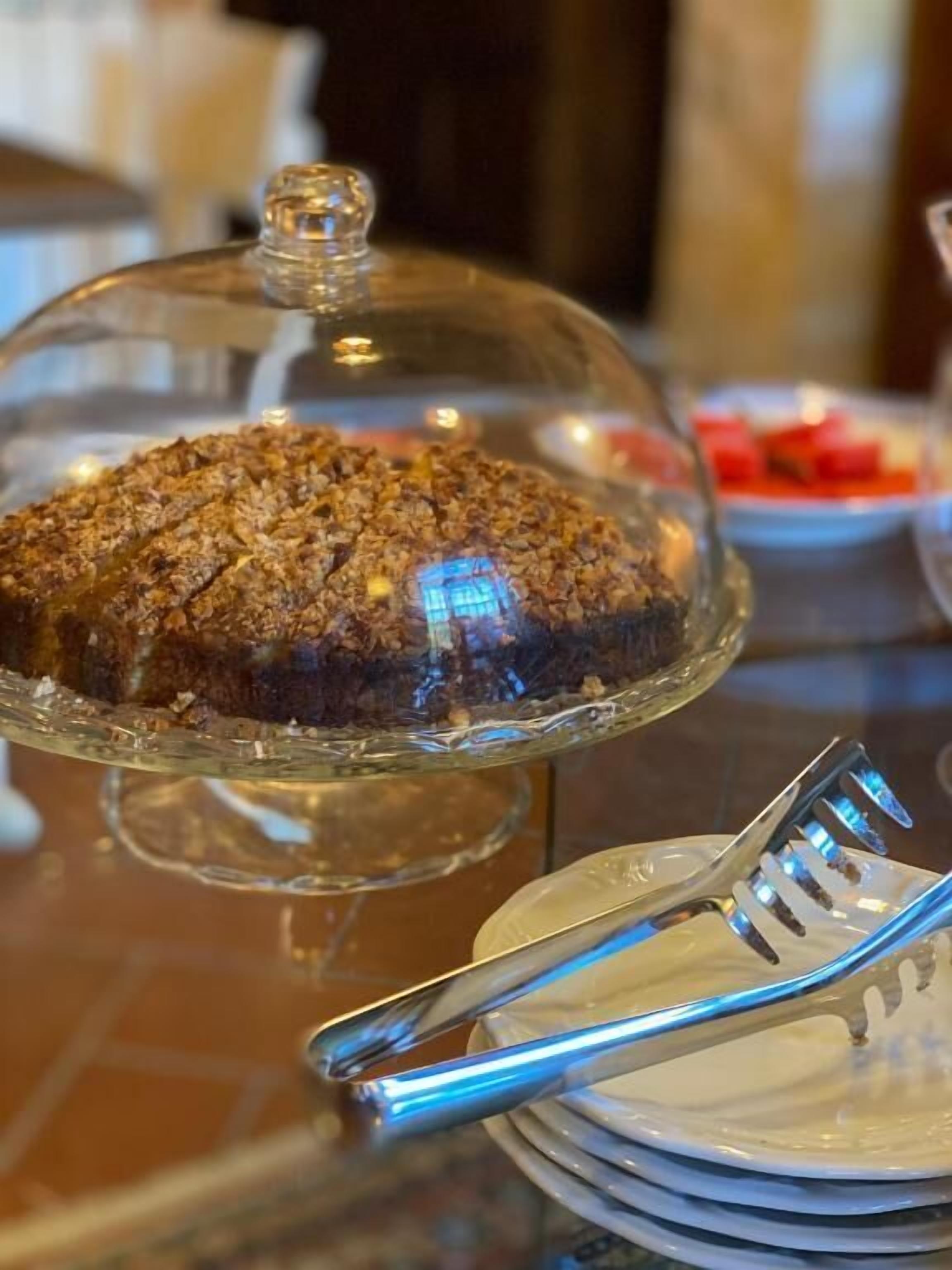 A dessert display with a covered cake on a glass stand, accompanied by a plate and a fork.