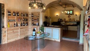 A rustic interior with wooden shelves displaying wine bottles, a glass table with a bottle and fruit, and a kitchen area visible through an archway. - Barco Mediceo (Carmignano)