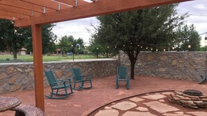 An outdoor patio with stone flooring, a fire pit, and green chairs.