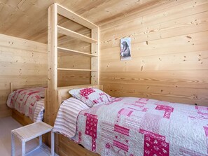 Une chambre dans une cabane en bois, avec un lit superposé, une petite table et une couvre-lit matelassé.
