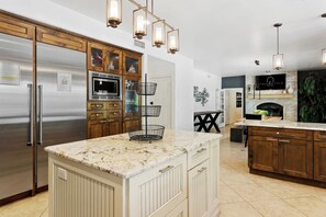 A kitchen with a large island, wooden cabinets, a stainless steel refrigerator, and a built-in oven.