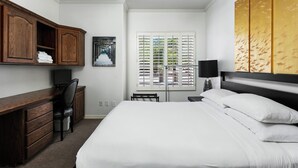 A hotel room with a bed, a desk, a chair, a window with blinds, and a ceiling fan.