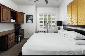 A hotel room with a bed, a desk, a chair, a window with blinds, and a ceiling fan.