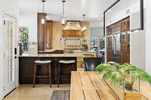 Une cuisine moderne dotée d’un îlot central, de meubles en bois, d’appareils électroménagers en acier inoxydable et de luminaires suspendus.