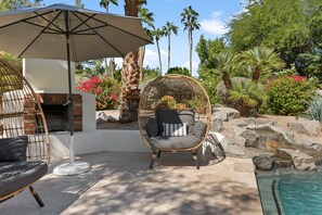 A patio area with a hanging chair, a grill, and a pool.