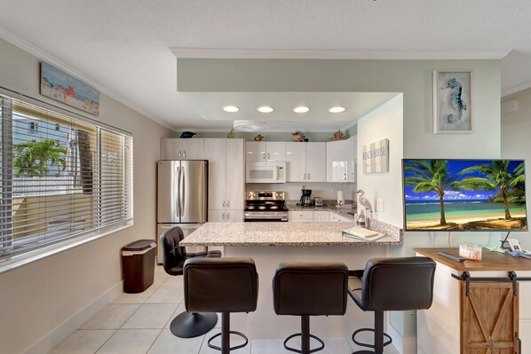 A modern kitchen with a central island, bar stools, and a large TV displaying a beach scene.