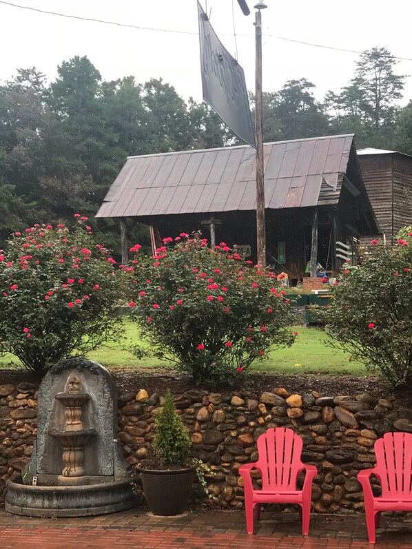 A rustic building with a metal roof, surrounded by a stone wall and blooming red flowers.