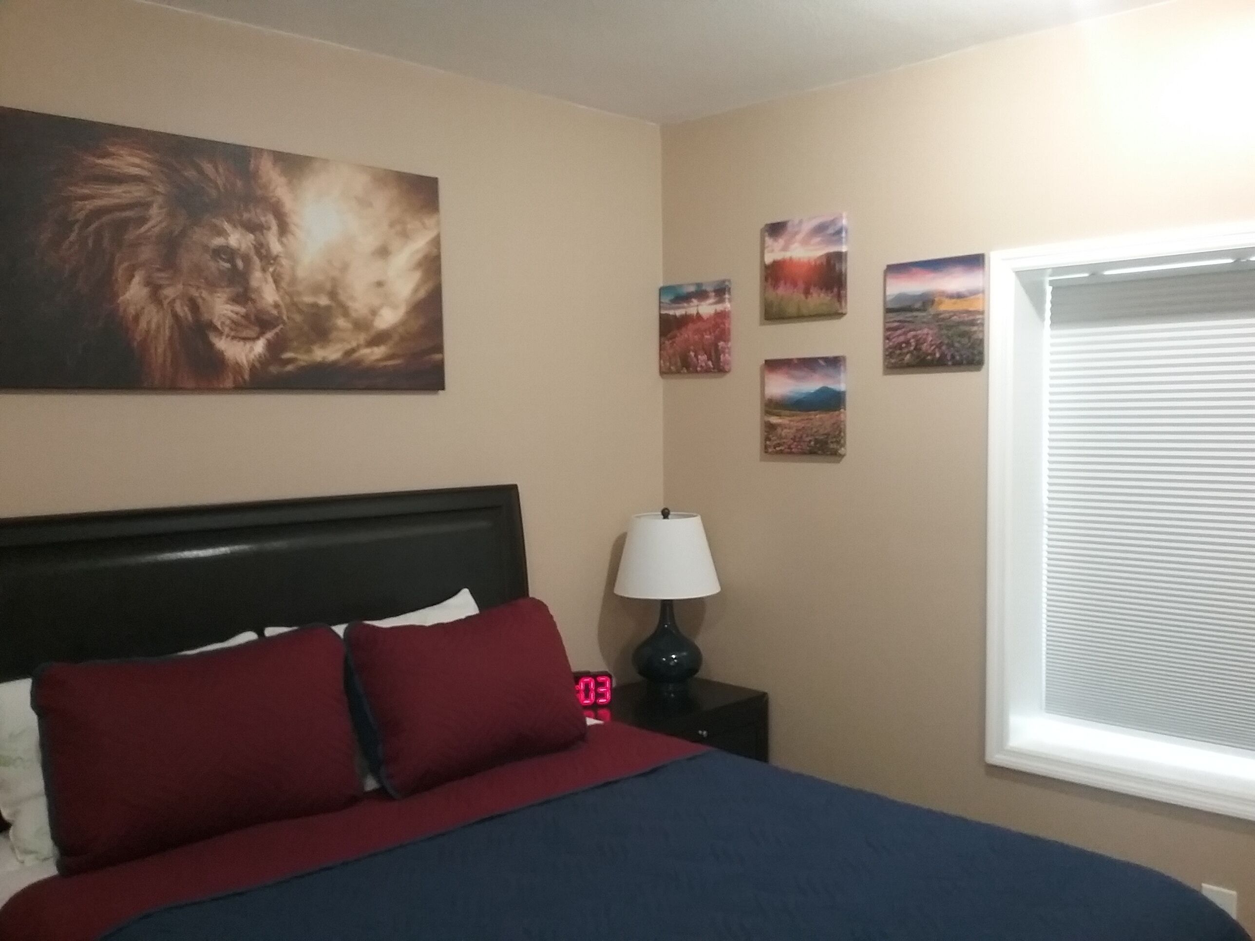 A bedroom with a bed, a nightstand, a lamp, and four wall-mounted pictures.