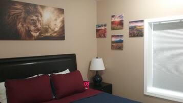 A bedroom with a bed, a nightstand, a lamp, and four wall-mounted pictures.